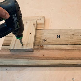 Litet växthus mot vägg: Brädorna till de lutande gavlarna (M) sätts ihop Litet växthus mot vägg: Brädorna till de lutande gavlarna (M) sätts ihop